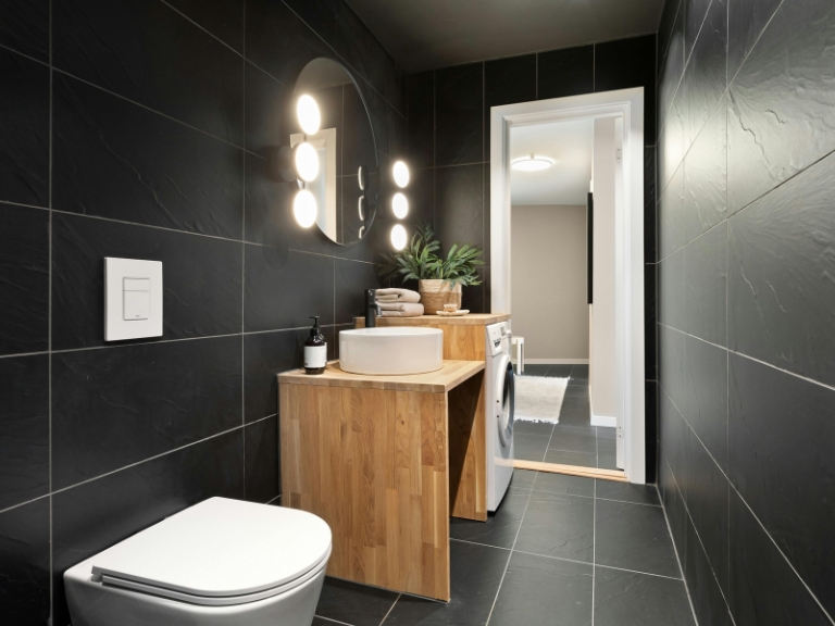 Łazienka z czarnymi płytkami i drewnianą szafką pod umywalką