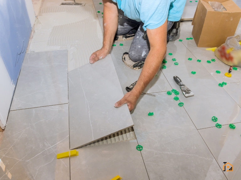 Glazurnik układający płytki na podłodze z użyciem poziomicy i klipsów dystansowych